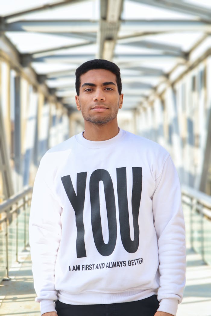 Portrait of a stylish man in a sweatshirt standing on a modern bridge.