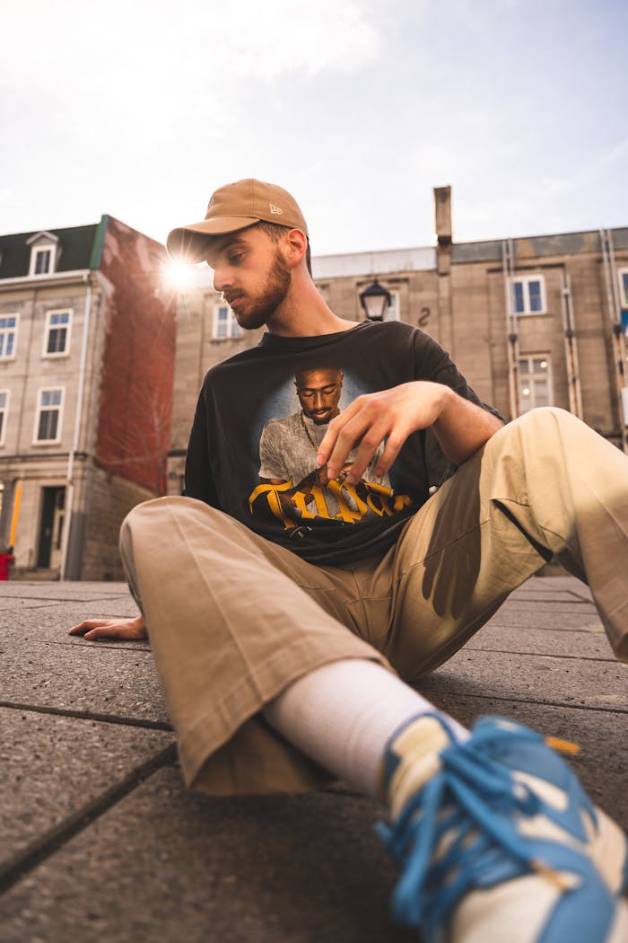 Low angle urban portrait of a young man in trendy fashion sitting on a city street.