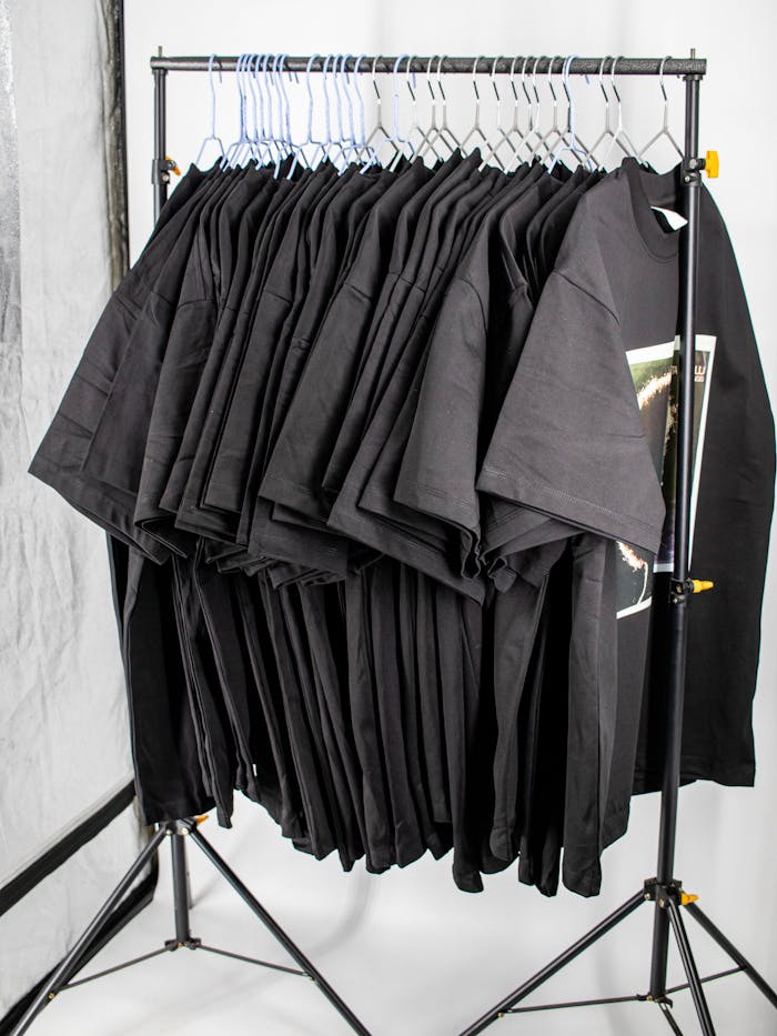 Home Collection of plain black t-shirts neatly hung on a metal rack in a professional studio setting.